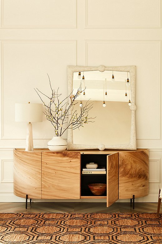 The entry is a time-honored place for a mirror, so that you can check once more before heading out that you look marvelous. Here, the visual weight of the mirror on the right counters that of the double team of lamp and vase on the left, providing balance without symmetry. Find the sideboard here, the rug here, and the lamp here. 
